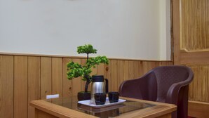 A wooden-paneled room with a glass table set for two, featuring a small bonsai tree, a stainless steel coffee pot, and two black mugs. - Madhuvan 2BHK, W/ Food, parking, Mountain View (Manali)
