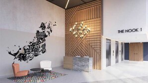 A modern lobby with a geometric ceiling design, a wooden accent wall, a chandelier, and a reception desk labeled "THE NOOK 1".