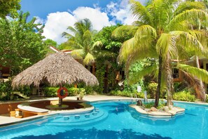 A resort pool area with a thatched umbrella, palm trees, and a clear blue sky. - Cocomarindo Breeze Condo and Amazing Pool (Coco)