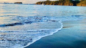 Une plage aux eaux calmes, un ciel dégagé et des bateaux à l’horizon.