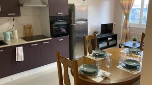A modern kitchen with a refrigerator, oven, and a dining area with a table set for two. - LES IRIS ANNEMASSE (Annemasse)