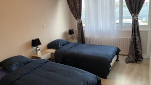 A hotel room with two beds, a nightstand with a lamp, and a window with curtains. - LES IRIS ANNEMASSE (Annemasse)