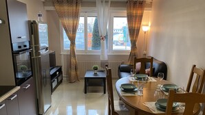 A modern kitchen with a built-in oven, a refrigerator, and a dining area with a wooden table set for four. - LES IRIS ANNEMASSE (Annemasse)