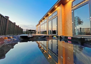 Um edifício moderno com grandes janelas, fachada de madeira e uma piscina refletora.