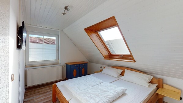 Une chambre avec un plafond en pente, un puits de lumière, un lit, une armoire et un radiateur.