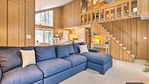 A modern living room with a blue sectional sofa, wooden walls, and a staircase leading to an upper level.