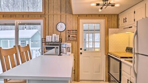 A kitchen with a wooden interior, white cabinets, a white refrigerator, a stove, and a dining area with wooden chairs and a white table.