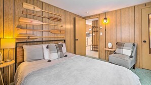A hotel room with a wooden paneled wall, a bed with white bedding, a chair, a small table with a lamp, and a wall-mounted mirror.