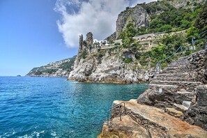 Eine Küstenlandschaft mit einem felsigen Klippen, einer Treppe, die zu einem Gebäude führt, und einem klaren, blauen Meer.