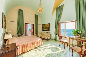 Ein Zimmer mit Bett, einer Couch, einem Esstisch mit Stühlen, einer Chandelier und Meerblick.