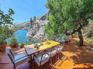 Eine Terrasse mit Esstisch mit Blick auf eine Küstenklippe und das Meer.