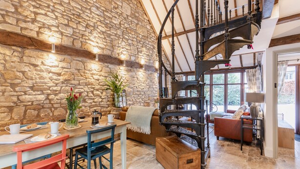 Un intérieur rustique avec un mur en pierre, un escalier en bois et un coin salon confortable avec une table et des chaises.