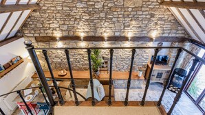 Un plafond en pierre avec des poutres en bois, un escalier avec des balustrades noires, un coin repas avec une table et des chaises, et une cheminée.