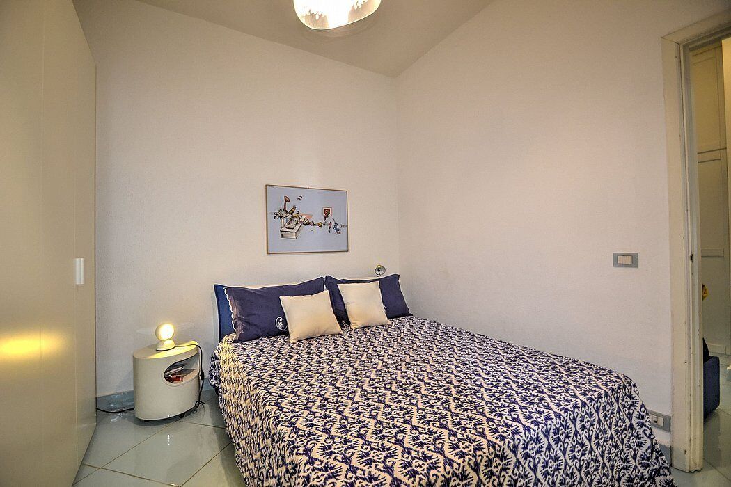 Ein Schlafzimmer mit einem Bett, einem Nachttisch, einem Wandbild und einer Tür rechts.
