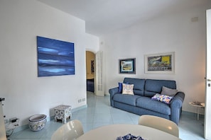 Uma sala de estar moderna com um sofá azul, uma mesa de jantar e uma área de cozinha.