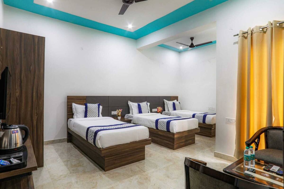 A hotel room with three beds, a coffee maker, a TV, and a desk with a chair.