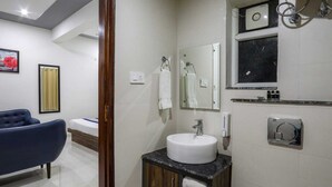 A modern bathroom with a white sink, a mirror, a towel rack, and a shower area. - KDS Residency (Greater Noida)