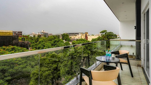 A balcony with a glass railing, two chairs, and a table with water bottles and a cup. - KDS Residency (Greater Noida)