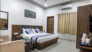 A hotel room with a bed, bedside tables, a mirror, a painting, an air conditioning unit, a window with curtains, and a coffee maker. - KDS Residency (Greater Noida)