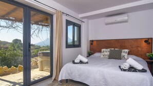 Une chambre à coucher avec un grand lit, une tête de lit en bois et une vue sur l’extérieur grâce à une porte-fenêtre coulissante.