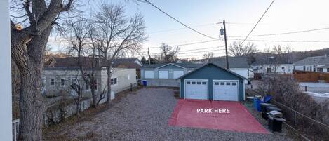 A residential area with a gravel driveway, a red parking area, and a small garage.