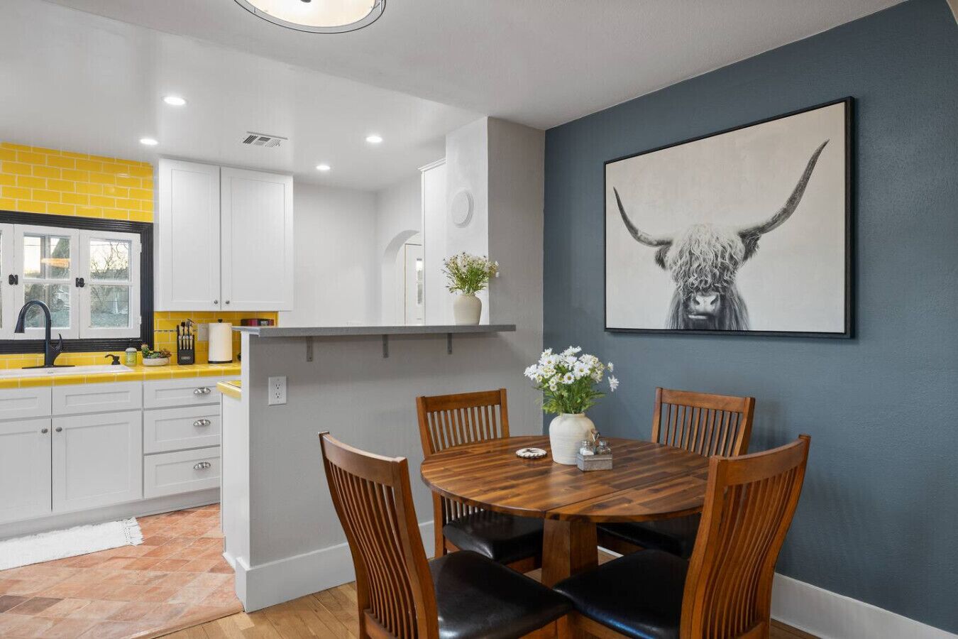 A dining area with a wooden table and chairs, a vase with flowers, and a bull's head artwork on the wall.
