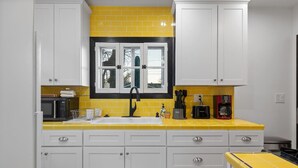 A kitchen with white cabinets, a yellow countertop, a black faucet, and a window above the sink.