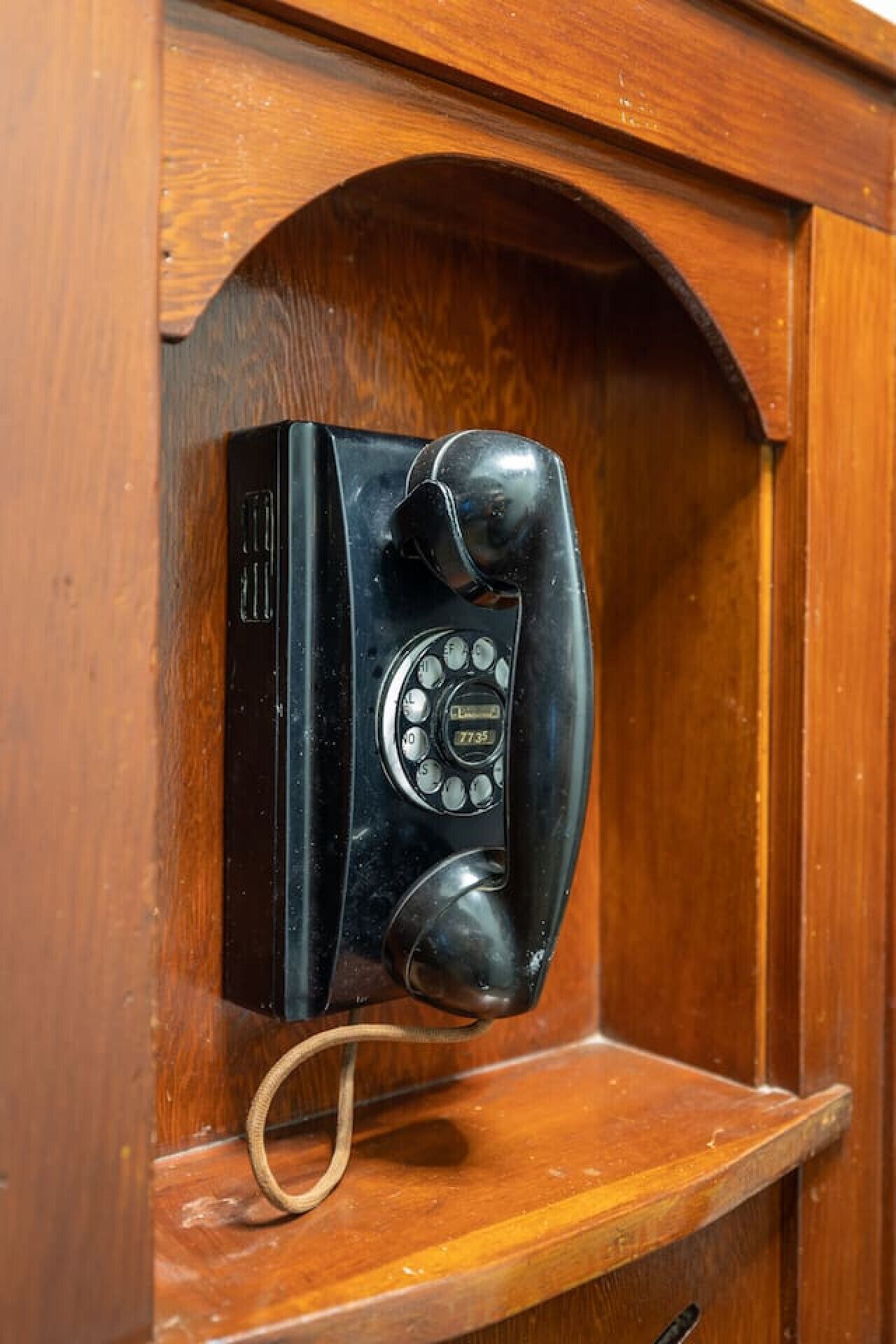 Un vieux téléphone à cadran rotatif, fixé sur un mur en bois.