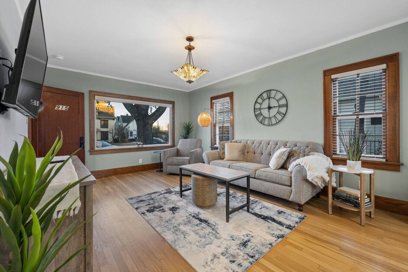 A living room with a sofa, armchair, coffee table, and a TV mounted on the wall.