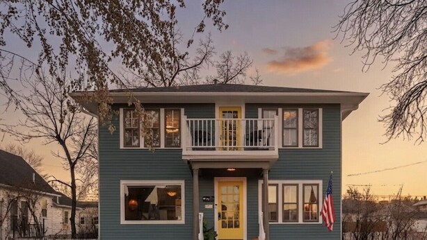 A two-story house with a front porch, a yellow door, and an American flag.