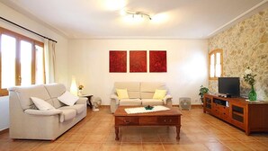 A living room with a beige sofa, a wooden coffee table, a TV on a wooden cabinet, and a stone wall. - CAN VILA with pool, A/C, Wifi, close to the beach, table tennis, outdoor barbecue (IB)