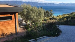 Une maison moderne avec une façade en bois, une allée pavée et une vue sur la mer et les montagnes en arrière-plan.