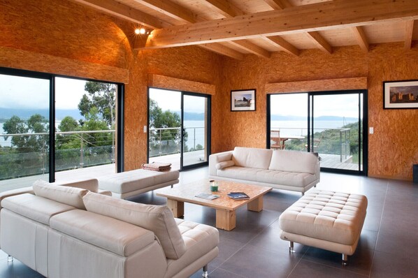 Amplia sala de estar con ventanas grandes, techo de madera y vista al mar.
