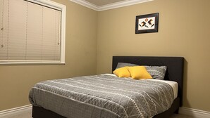 Een slaapkamer met een bed, een raam met zonwering en een ingelijst schilderij aan de muur.