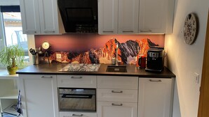 A modern kitchen with white cabinets, a built-in oven, a coffee maker, and a clock on the wall. - Modern studio in 1970s house in Haslital (Schattenhalb)