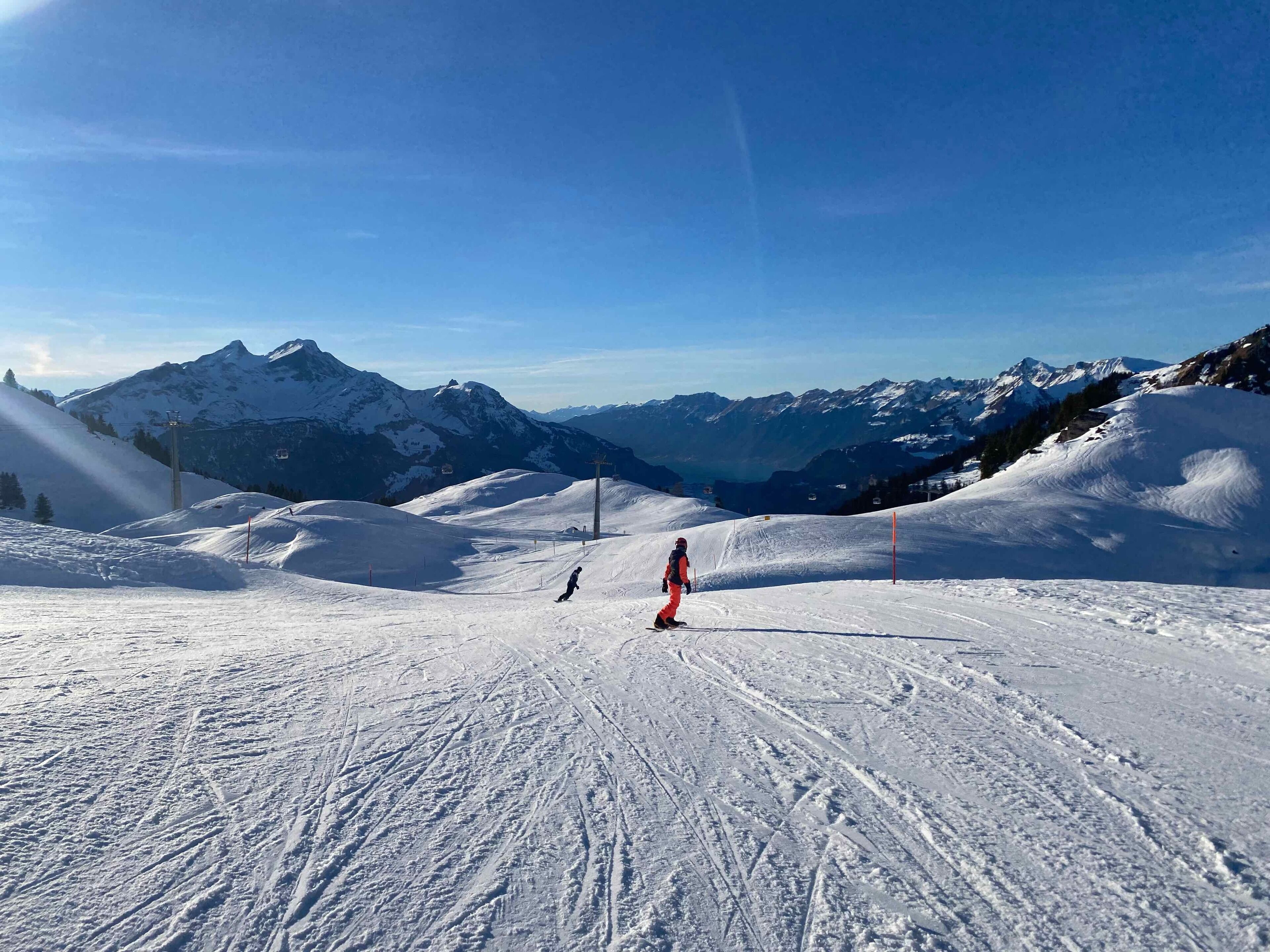 A snowy ski slope with a clear sky and mountains in the background.