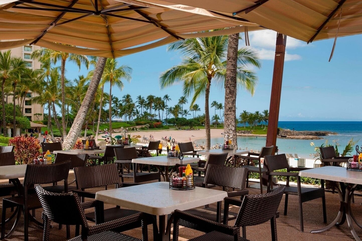 An outdoor dining area with tables and chairs, overlooking a beach and ocean.