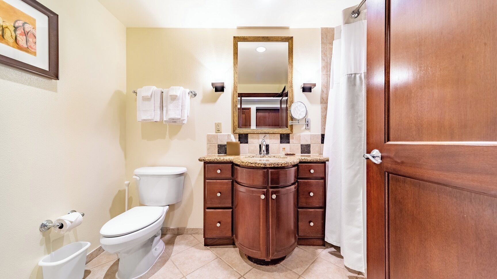 A bathroom with a toilet, sink, and mirror. There are towels hanging on the wall and a shower curtain.