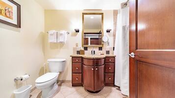 A bathroom with a toilet, sink, and mirror. There are towels hanging on the wall and a shower curtain.