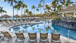 A pool area with lounge chairs, palm trees, and a view of the ocean.