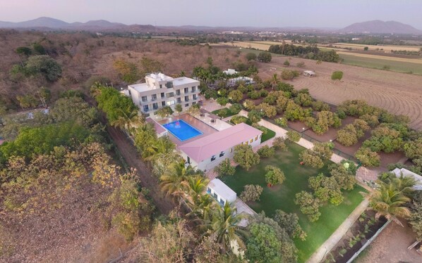 An aerial view of a hotel with a swimming pool, surrounded by landscaped gardens and palm trees. - Anantam Resort (Mendarda)