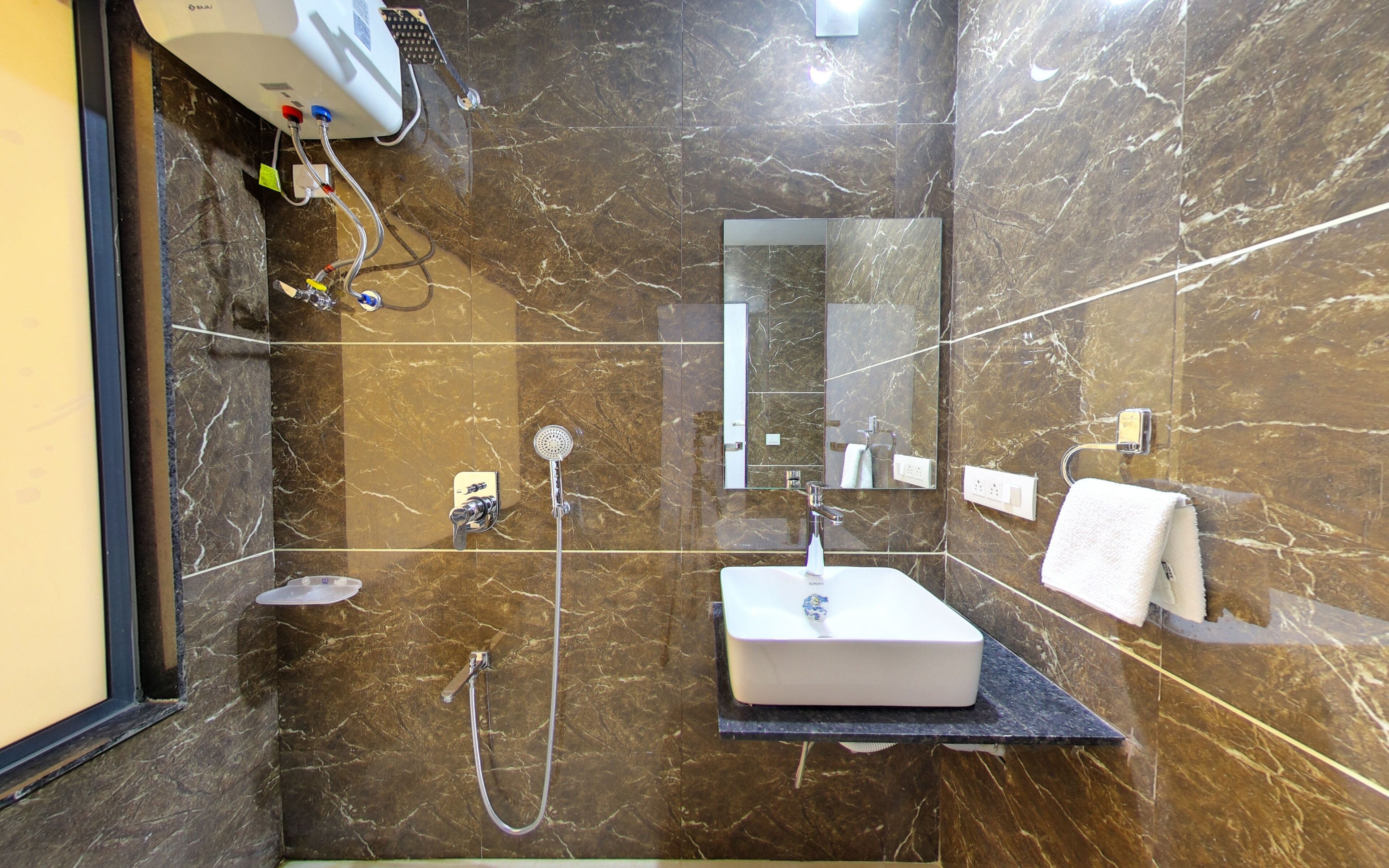 A modern bathroom with a marble floor, a built-in sink, a handheld showerhead, and a towel rack.