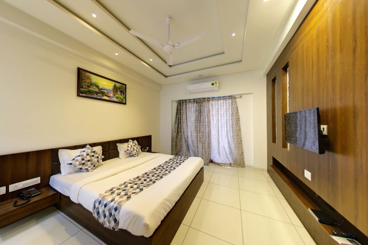 A hotel room with a large bed, a ceiling fan, an air conditioning unit, a television mounted on the wall, and a painting on the wall.