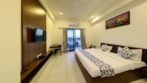 Una habitación de hotel con cama, escritorio, televisión y balcón con cortinas.