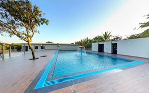 A swimming pool with a water feature, surrounded by a wooden deck and a white wall with doors. - Anantam Resort (Mendarda)