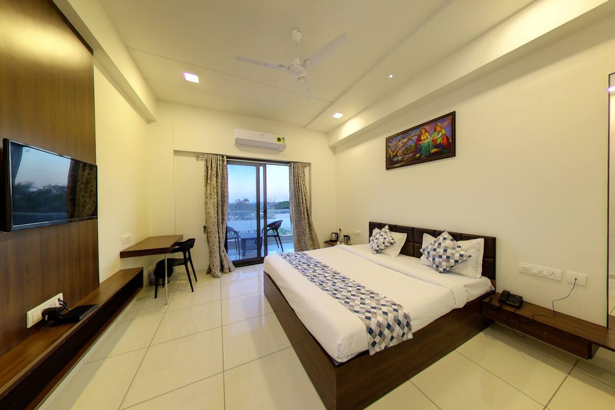 A hotel room with a bed, a desk, a chair, a TV, and a painting on the wall.