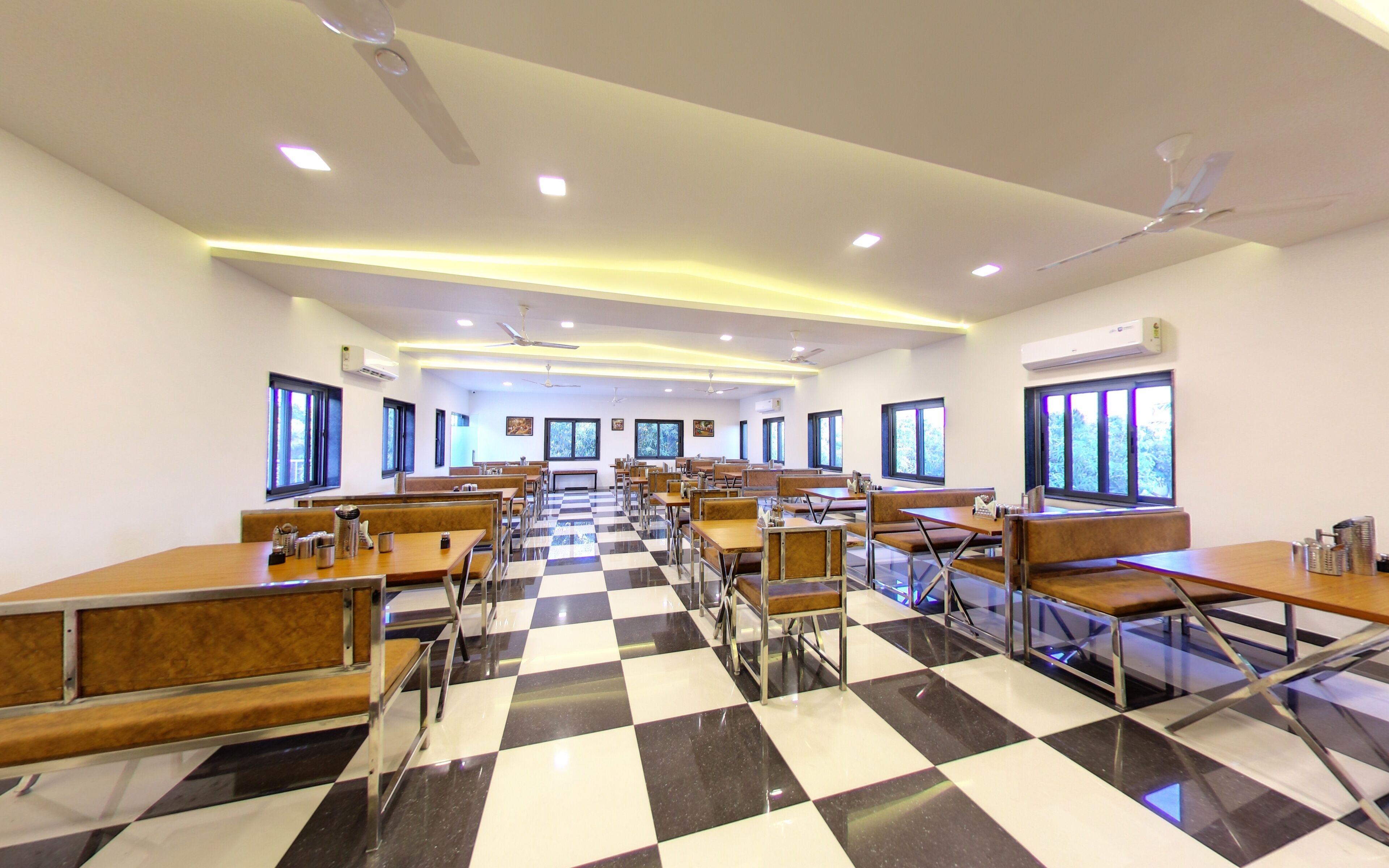 A cafeteria with checkered flooring, multiple tables and benches, ceiling fans, and large windows.