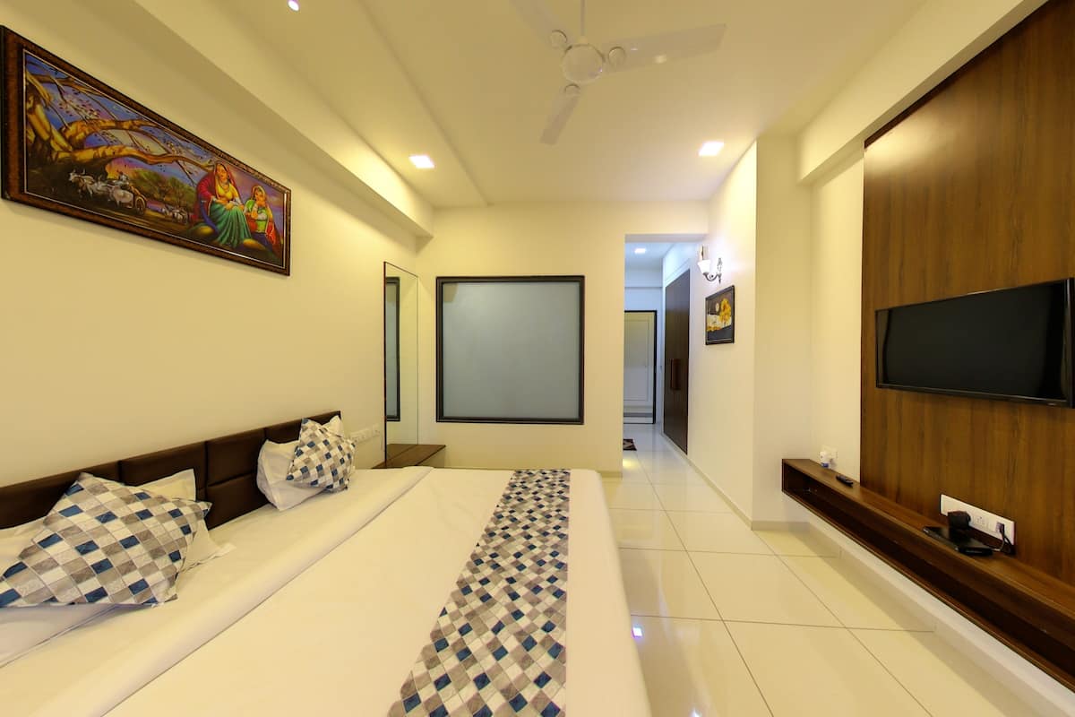A hotel room with a bed, a TV, a ceiling fan, a painting, and a wooden wardrobe.