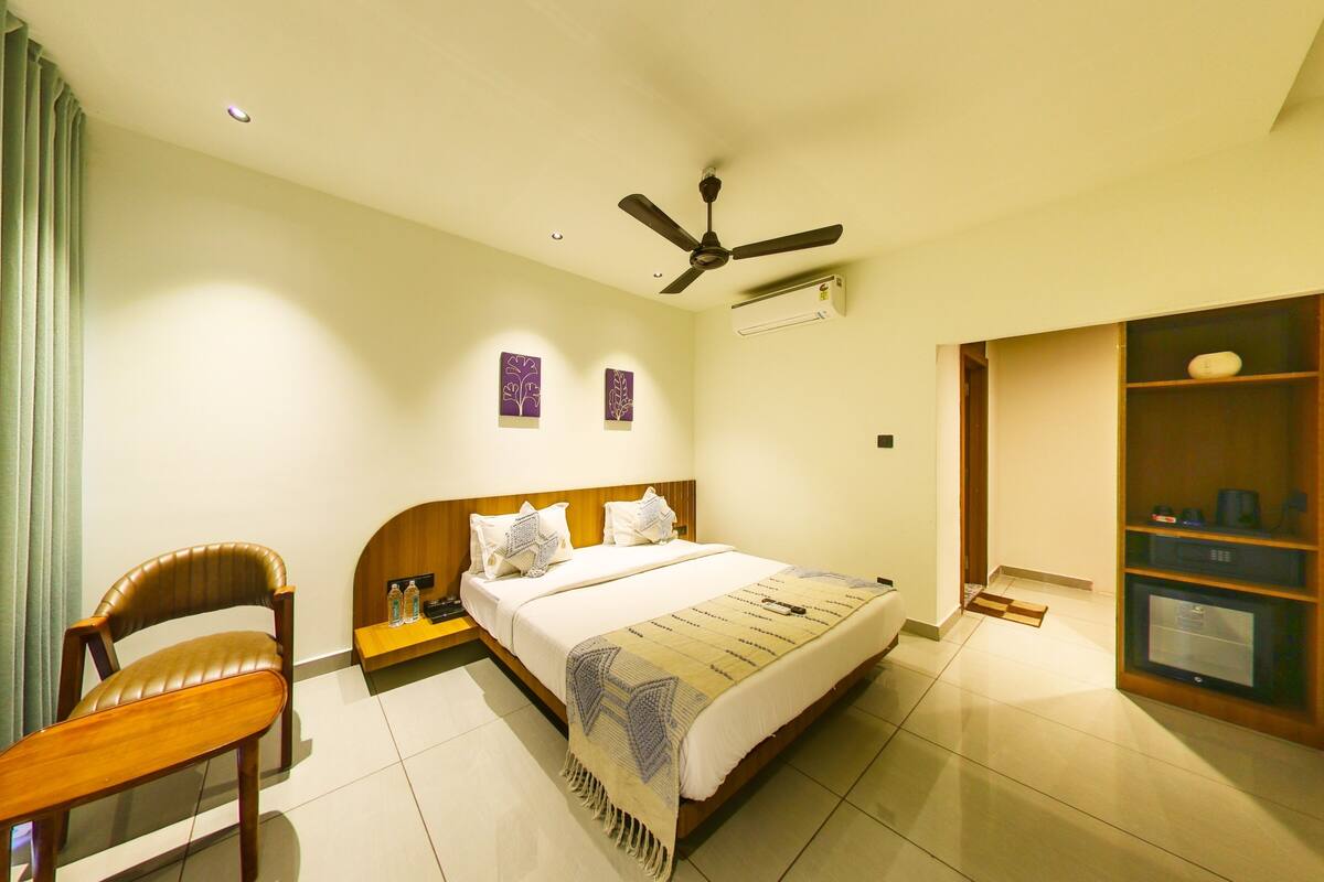A hotel room with a bed, a chair, a ceiling fan, a small table, and a wardrobe.
