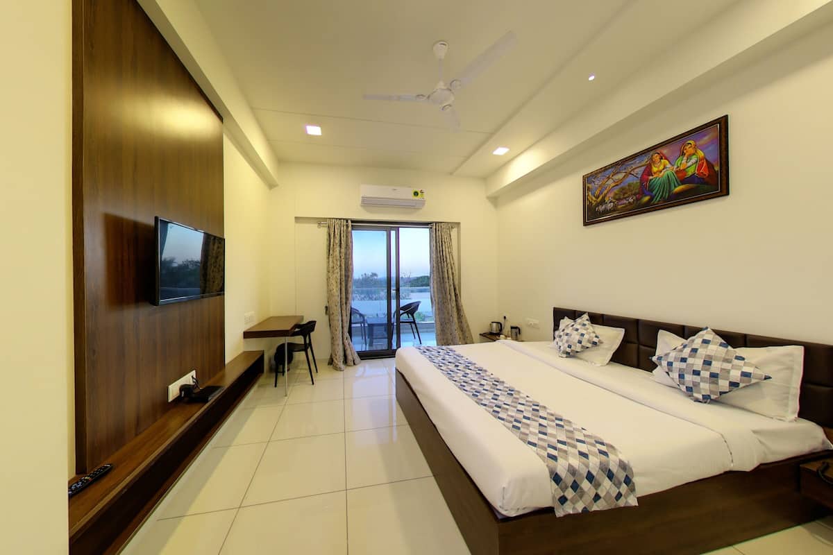 A hotel room with a bed, a TV, a desk, and a balcony with curtains.